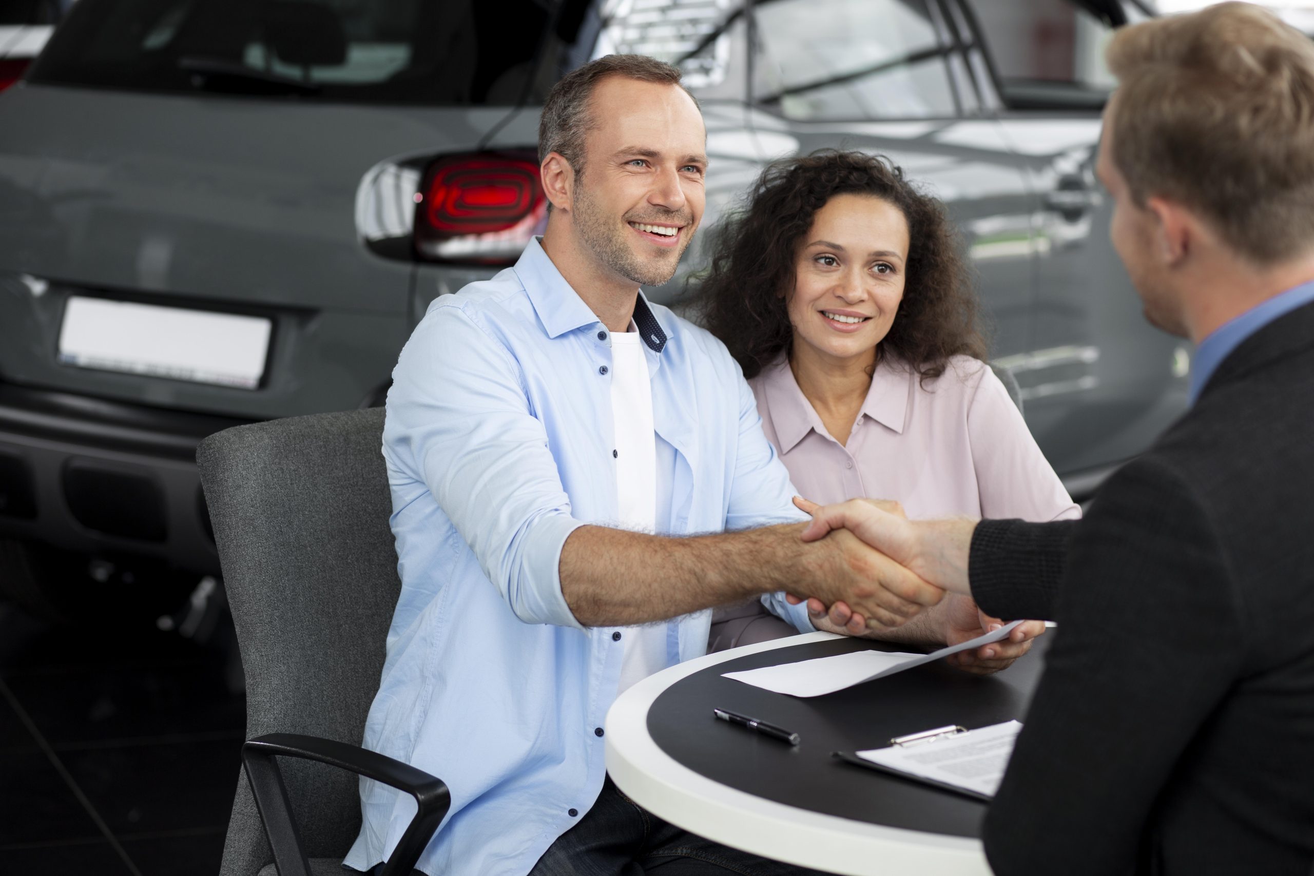 Vendedor de concesionario cerrando un trato con dos personas gracias a los consejos sobre cómo vender un auto con éxito.